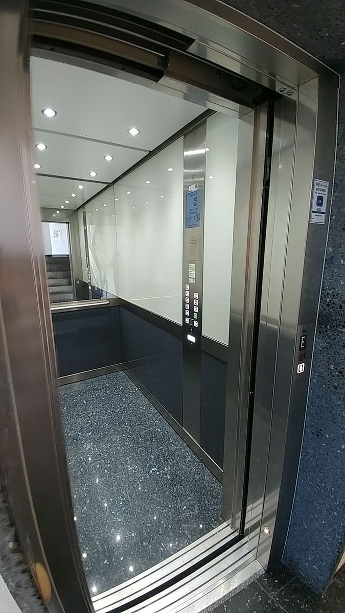 Offener Aufzug mit glänzendem, dunkelblauem Boden und weißen Wänden in einem modernen Gebäude